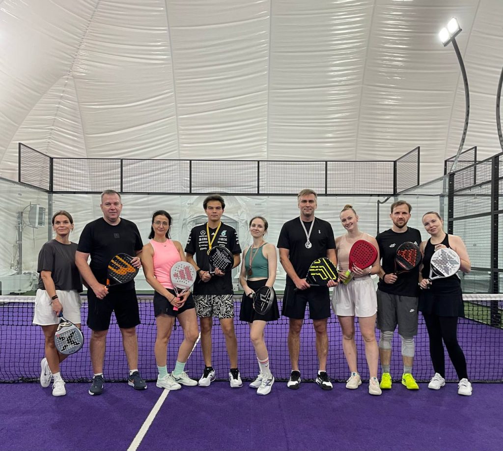 A group of players posing with rackets inside an indoor padel dome