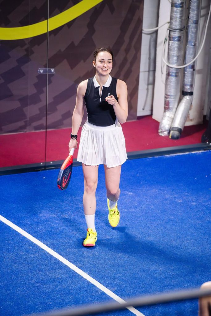 A female padel player walking onto a blue court with her racket