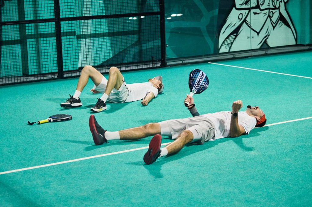A padel player resting on court with rackets