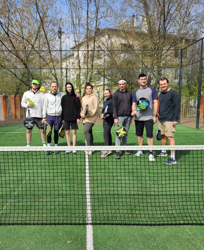 A group of players posing at the net of a padel court